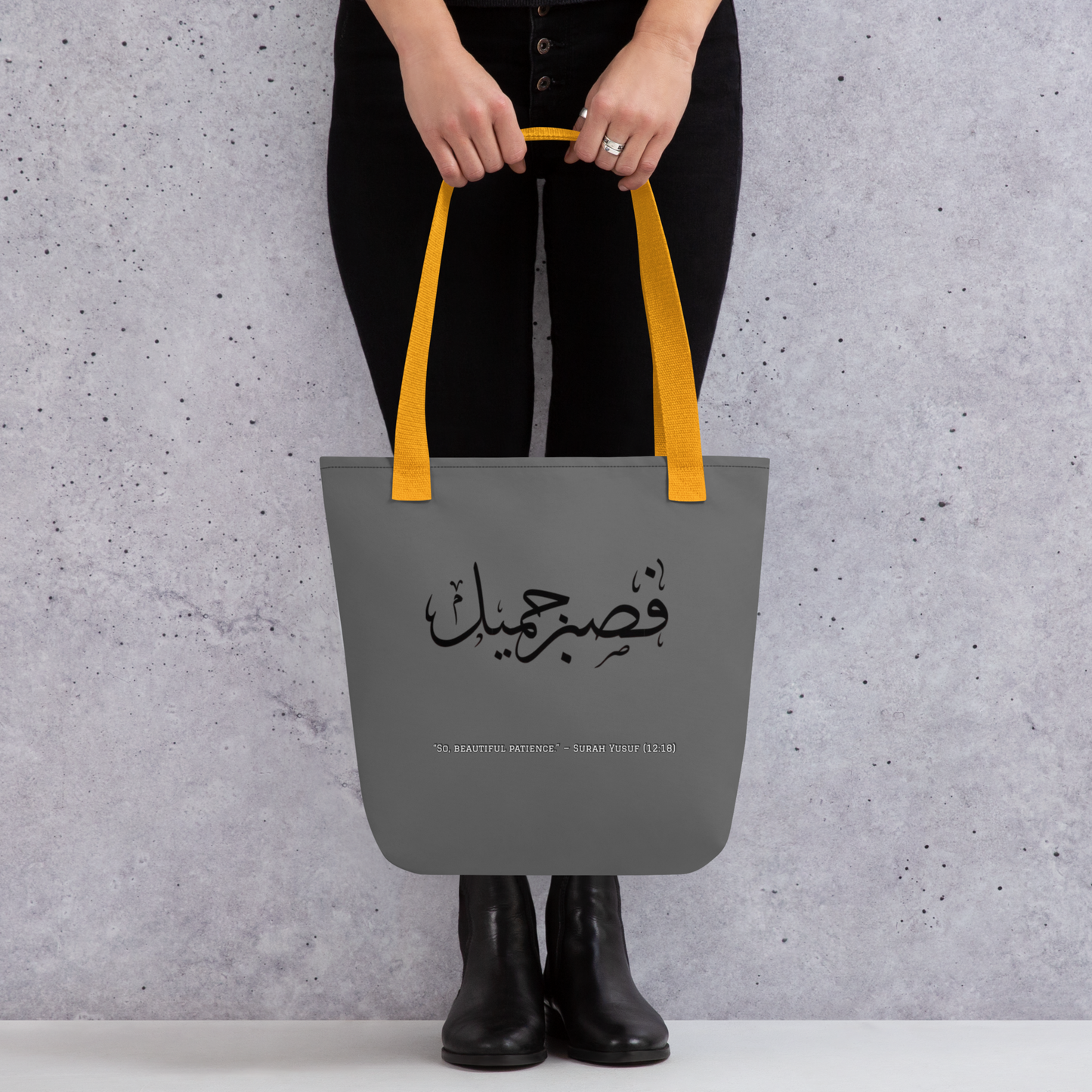 Person holding a gray tote bag with yellow handles against a gray background