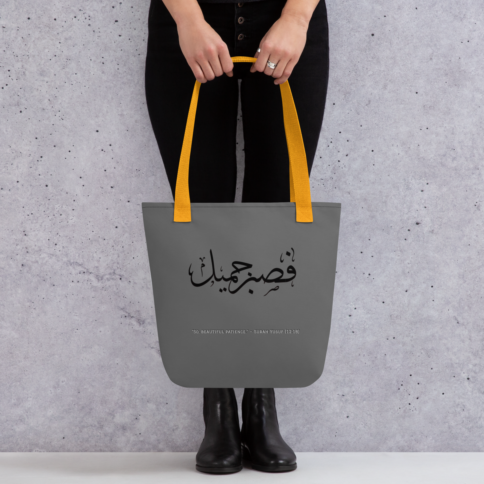 Person holding a gray tote bag with yellow handles against a gray background